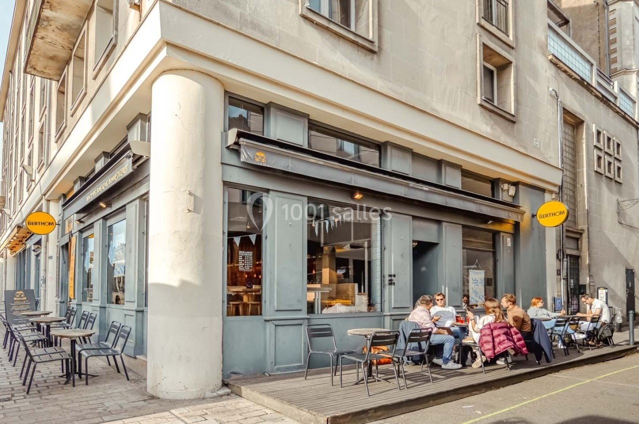 Façade d'un café avec terrasse, des clients assis à l'extérieur sur une rue urbaine ensoleillée.