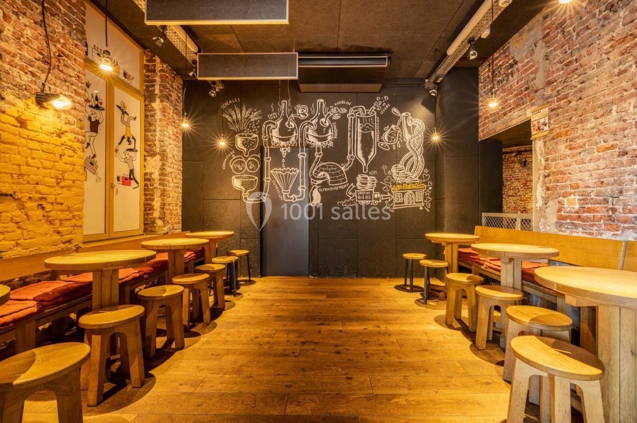 Salle de restaurant avec murs en briques, tables et tabourets en bois, et un mur décoré de dessins blancs.
