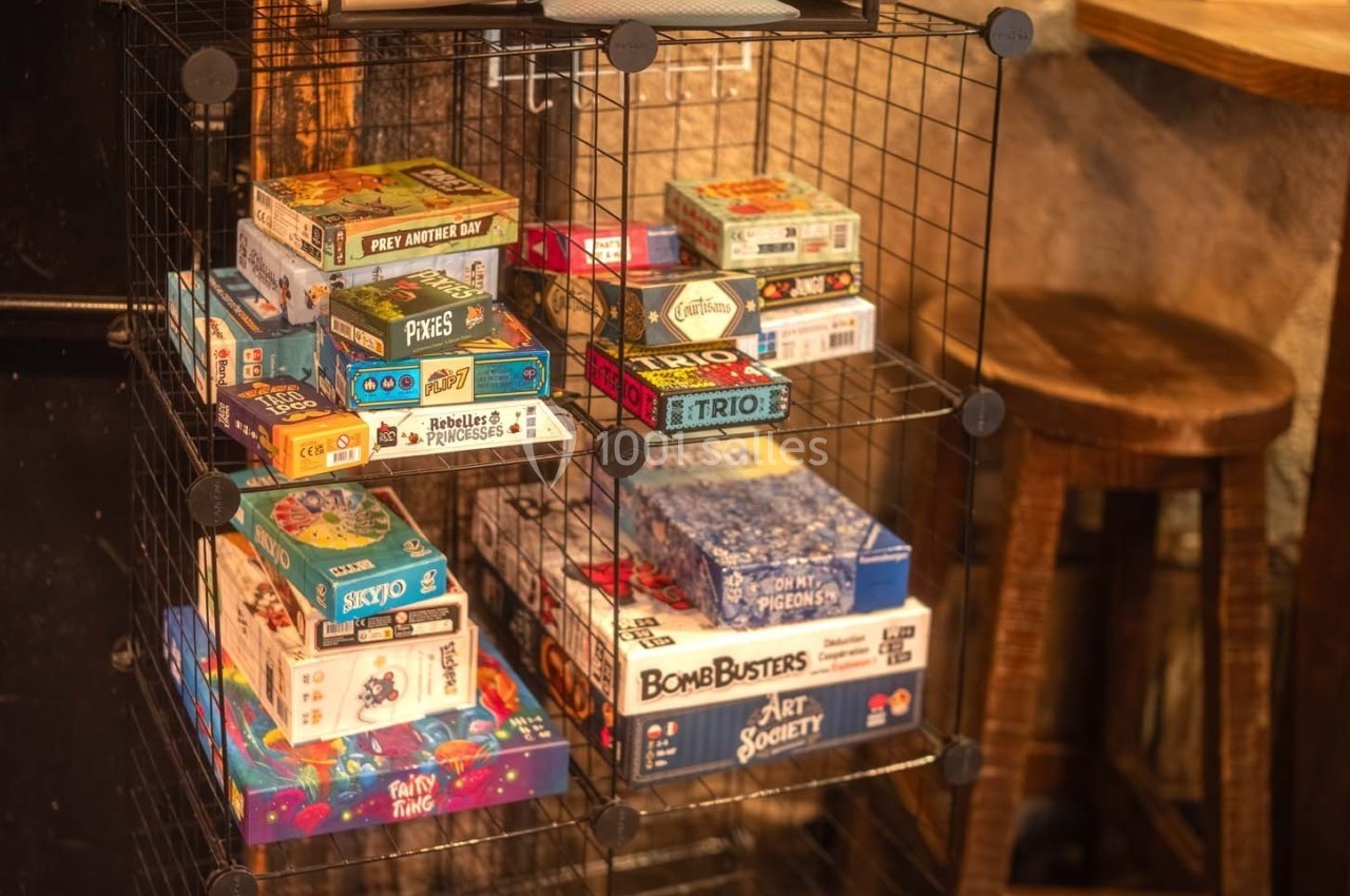 Jeux de société variés rangés sur des étagères en métal dans un espace intérieur chaleureux.