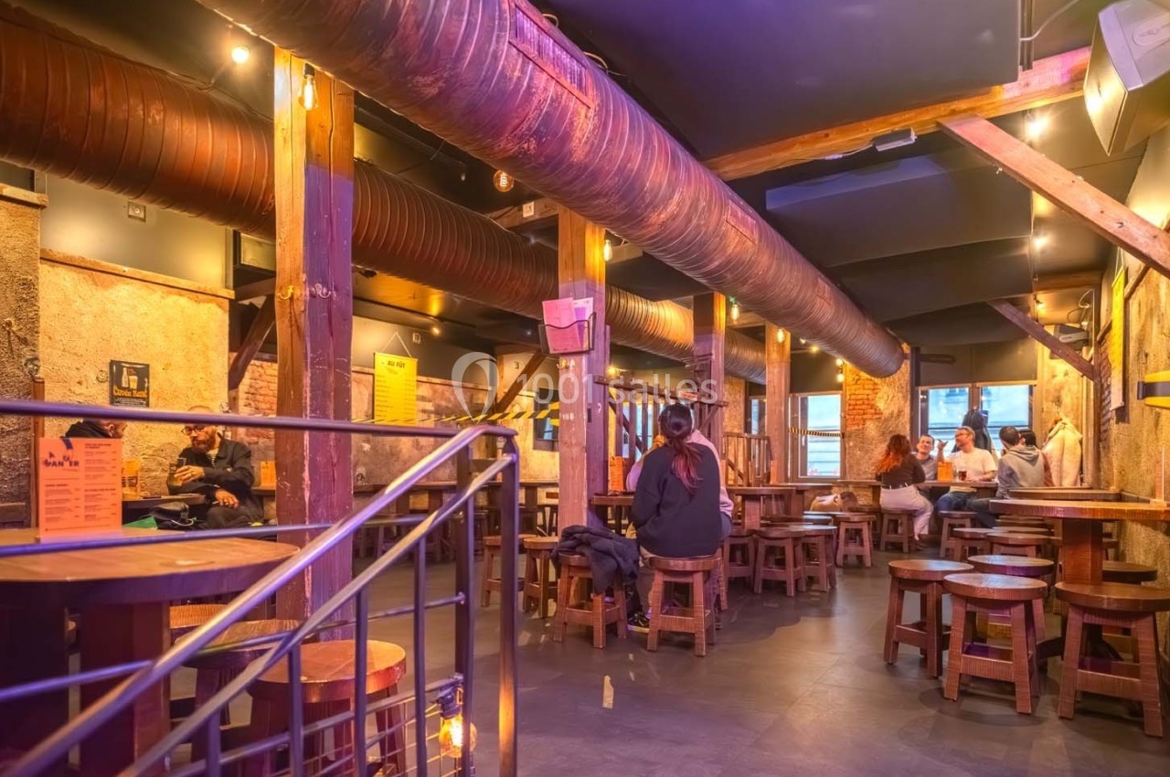 Intérieur d'un bar chaleureux avec des tables en bois, des poutres apparentes et des clients discutant.