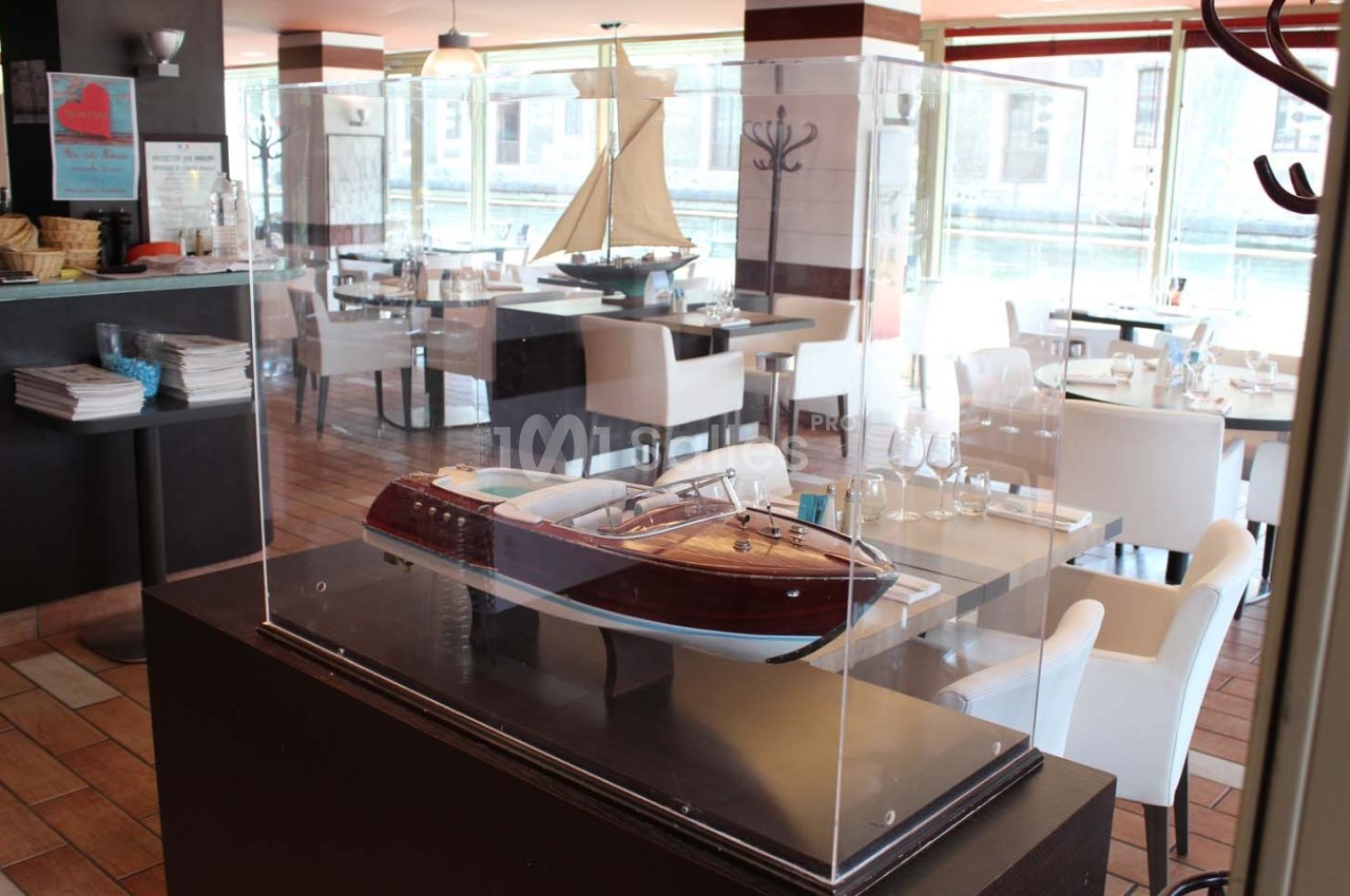 Maquette de bateau en bois exposée sous une vitrine dans un restaurant lumineux avec vue sur l'extérieur.