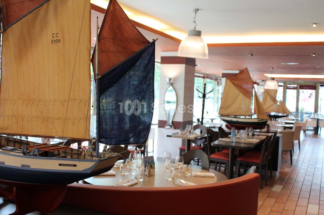 Maquettes de voiliers exposées dans un restaurant lumineux avec des tables dressées.