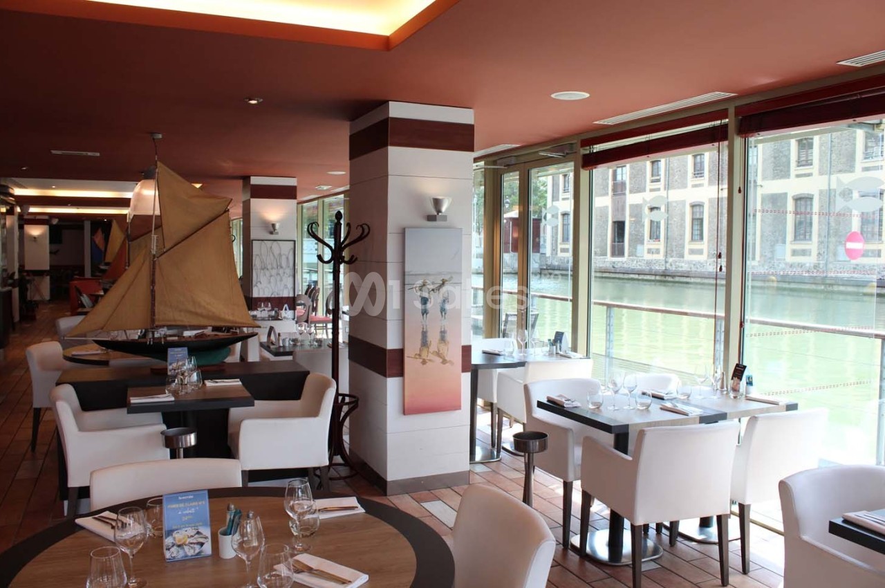 Salle de restaurant lumineuse avec vue sur un canal, tables dressées et décoration nautique.