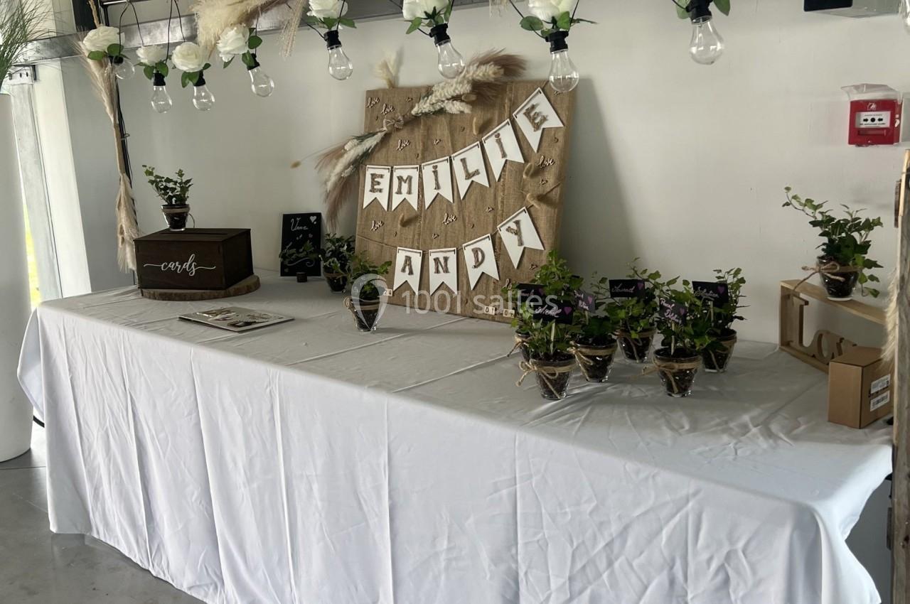 Table décorée pour un événement avec guirlande de fleurs, pots de plantes et une bannière ’Emilie Andy’.