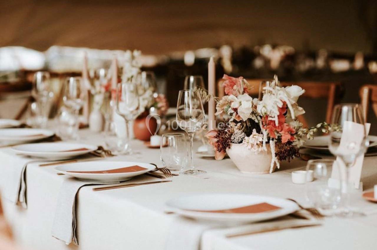 Table dressée avec une nappe beige, vaisselle blanche, verres en cristal et centre de table floral aux tons pastel.
