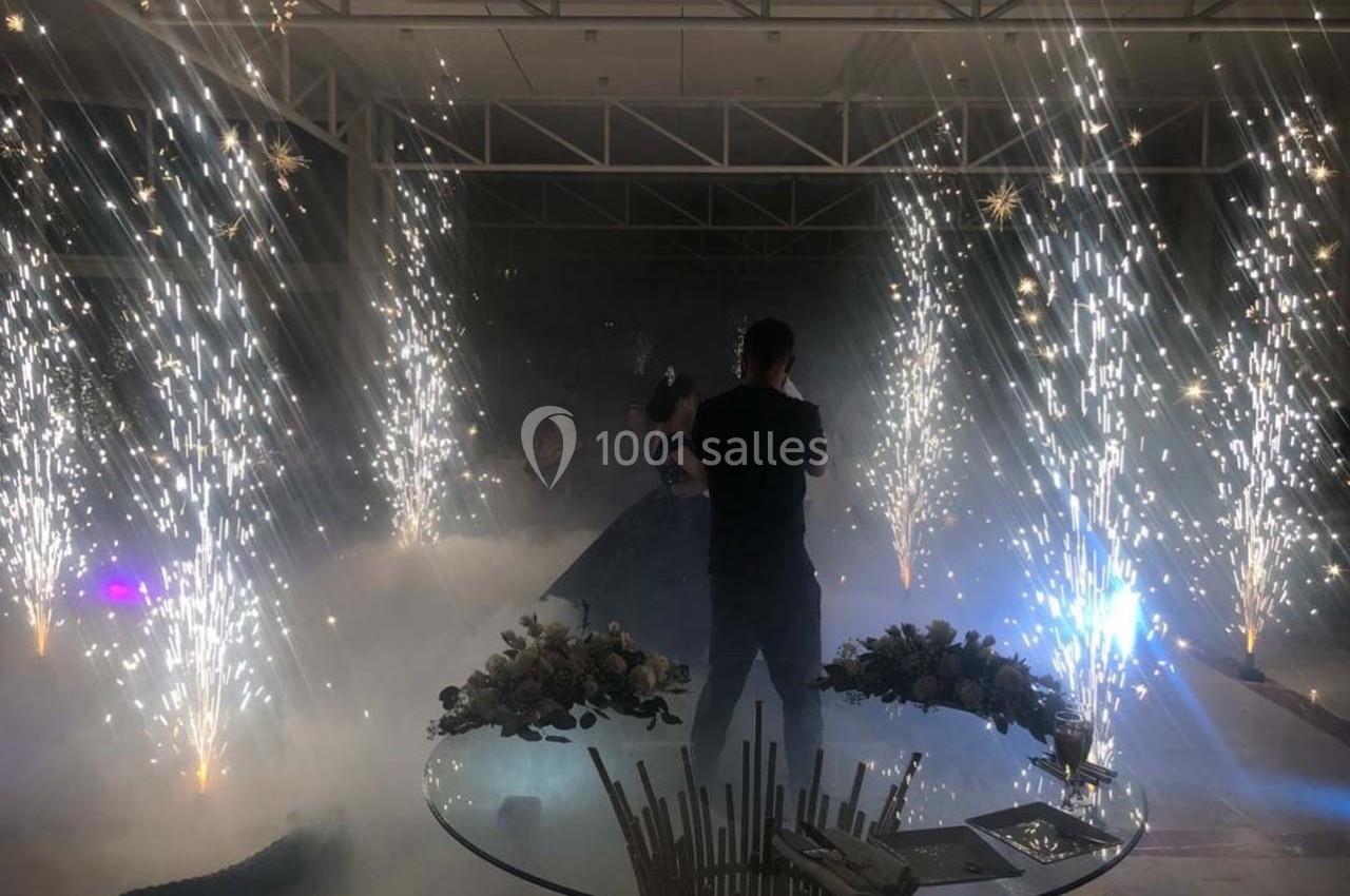 Un couple danse au centre d'une salle illuminée par des fontaines d'étincelles et entourée de fumée légère.