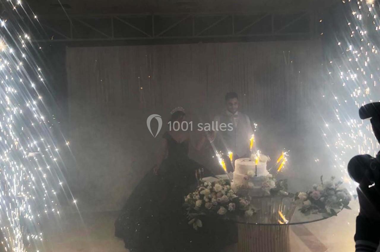 Un couple coupe un gâteau de mariage entouré d'étincelles et de décorations florales sur une table en verre.