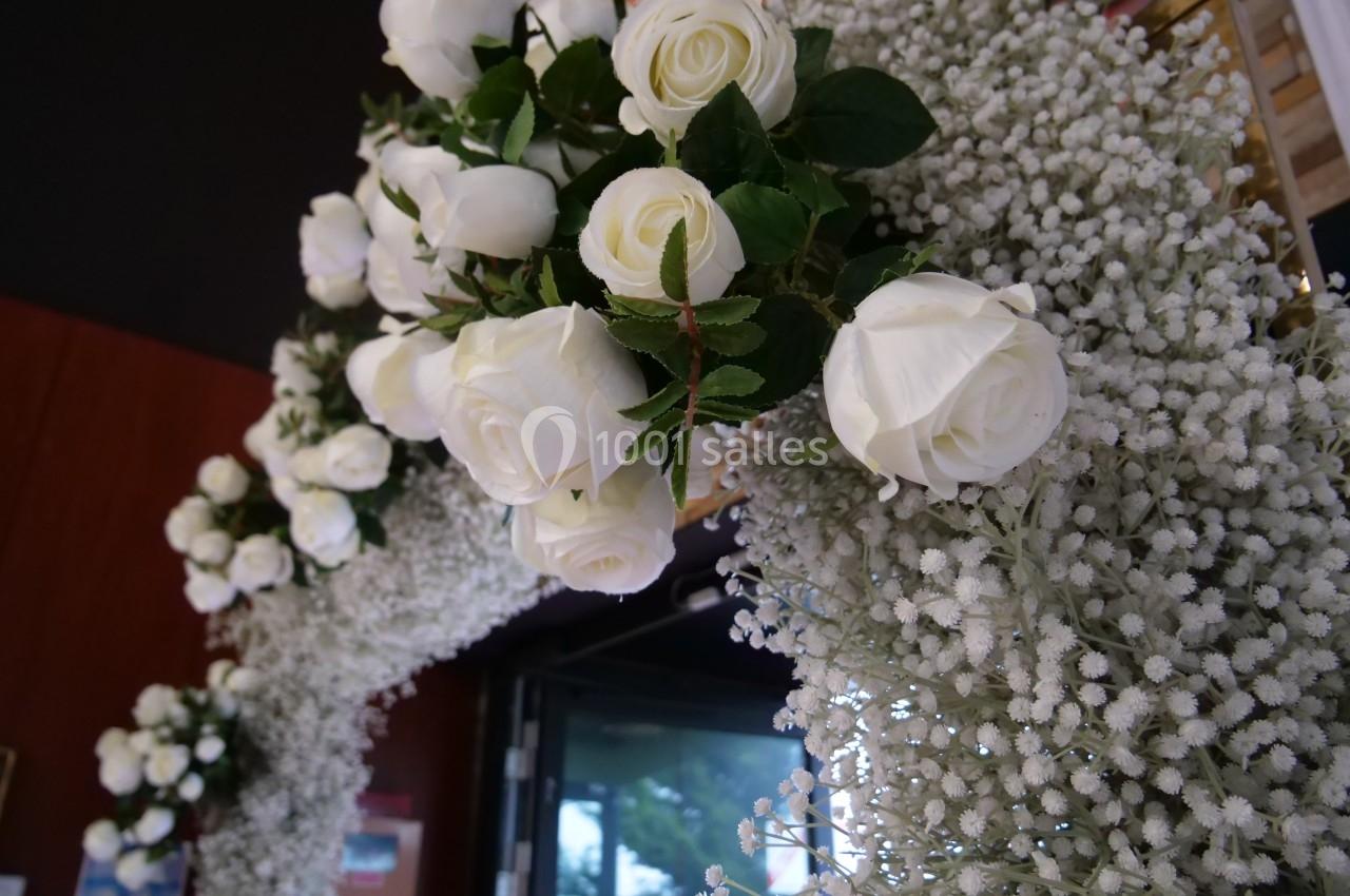 Arc décoratif orné de roses blanches et de gypsophiles, placé devant une entrée avec un fond sombre.