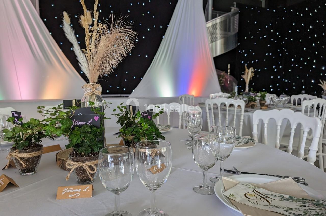 Tables décorées pour un événement avec nappes blanches, plantes en pot, verres et chaises blanches devant un fond étoilé.