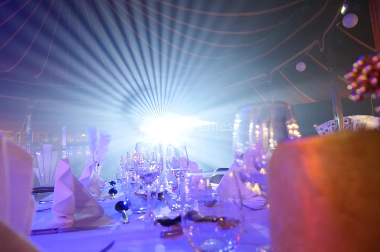 Table élégamment dressée avec des verres et serviettes, éclairée par une lumière vive dans une ambiance tamisée.