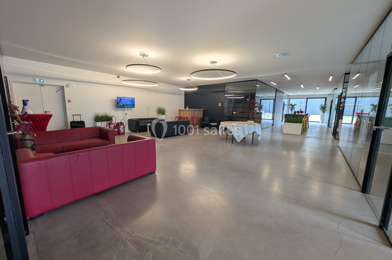 Salle lumineuse avec canapés rouges, tables décorées et grandes baies vitrées donnant sur l'extérieur.