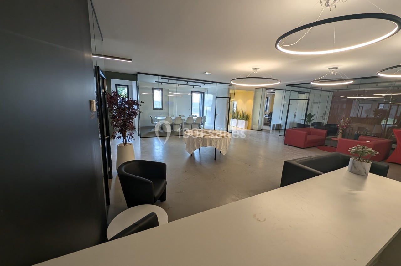 Espace intérieur moderne avec mobilier design, grande table ronde centrale et baies vitrées donnant sur plusieurs salles.