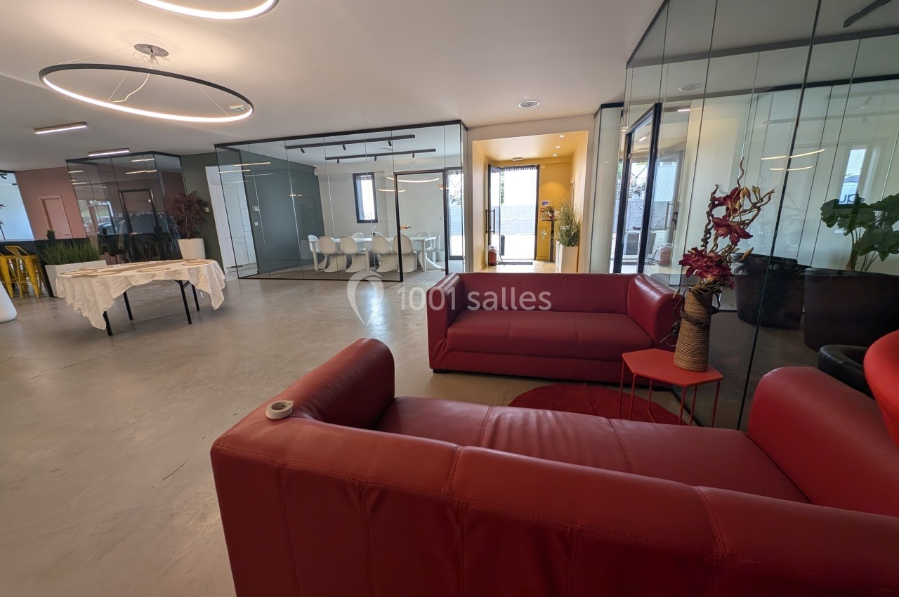 Espace moderne avec canapés rouges, table basse et murs vitrés donnant sur des salles de réunion lumineuses.