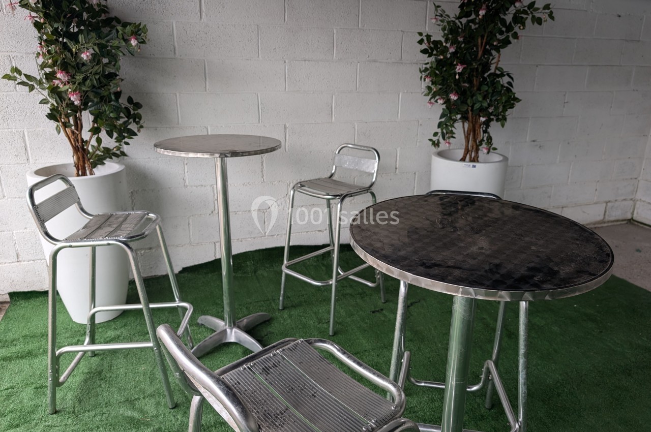 Tables et chaises en métal disposées sur un sol en gazon artificiel, avec des plantes en pots en arrière-plan.