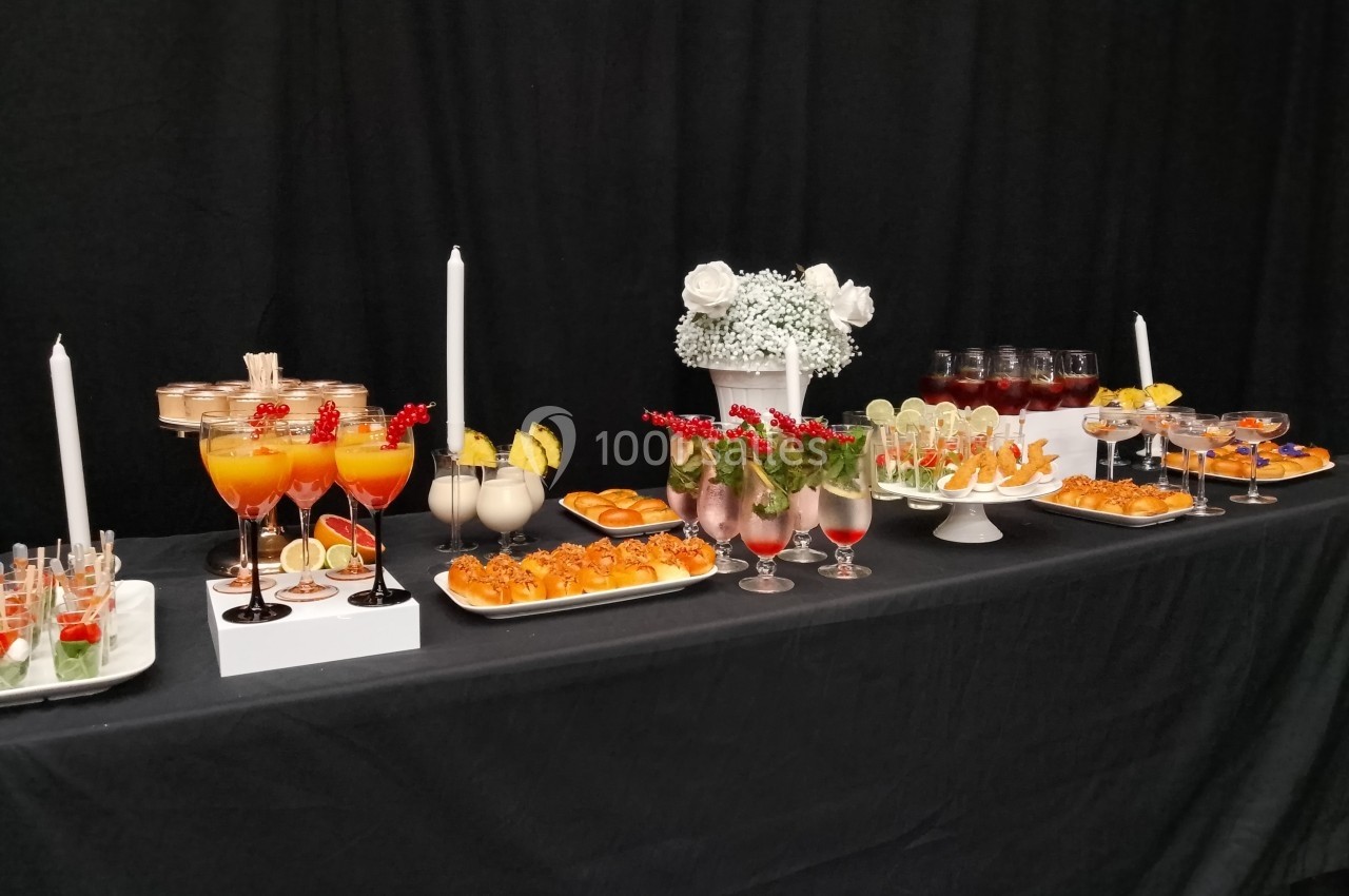 Buffet élégant avec cocktails colorés, verrines, fruits et décorations sur une nappe noire.