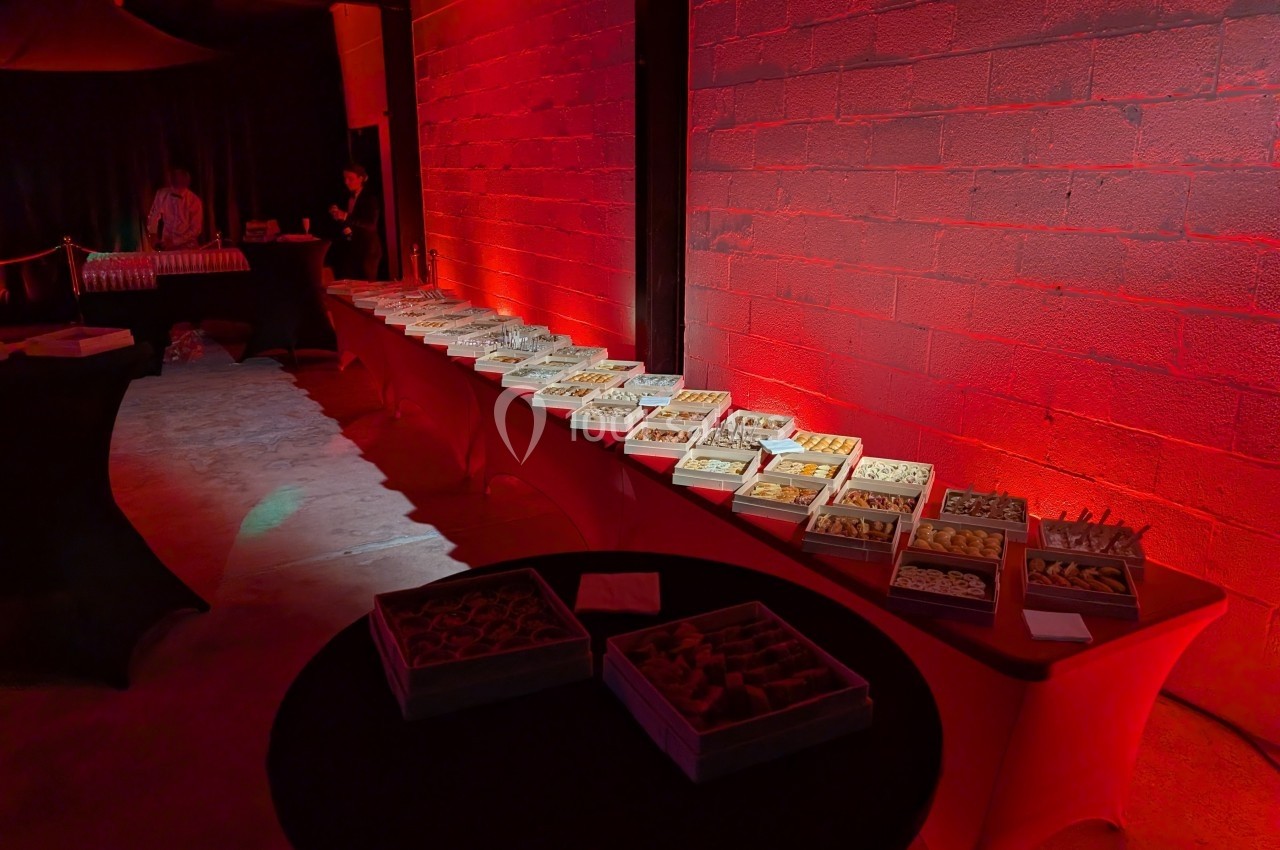 Buffet de petits fours disposés sur une longue table éclairée par une lumière rouge dans une salle sombre.