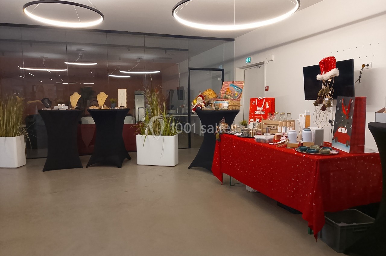 Salle décorée pour un événement avec des tables drapées, des plantes et une table rouge présentant divers objets.