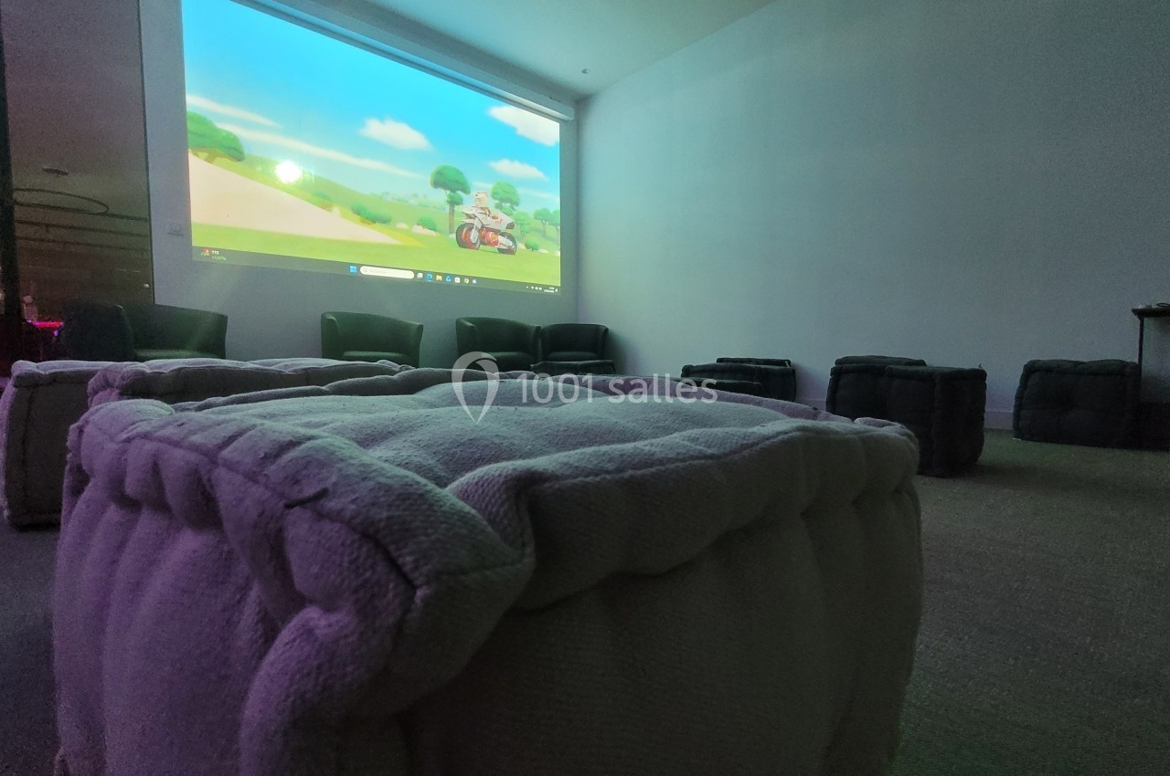 Projection d'un dessin animé sur un écran dans une salle avec des poufs et des fauteuils disposés pour les spectateurs.