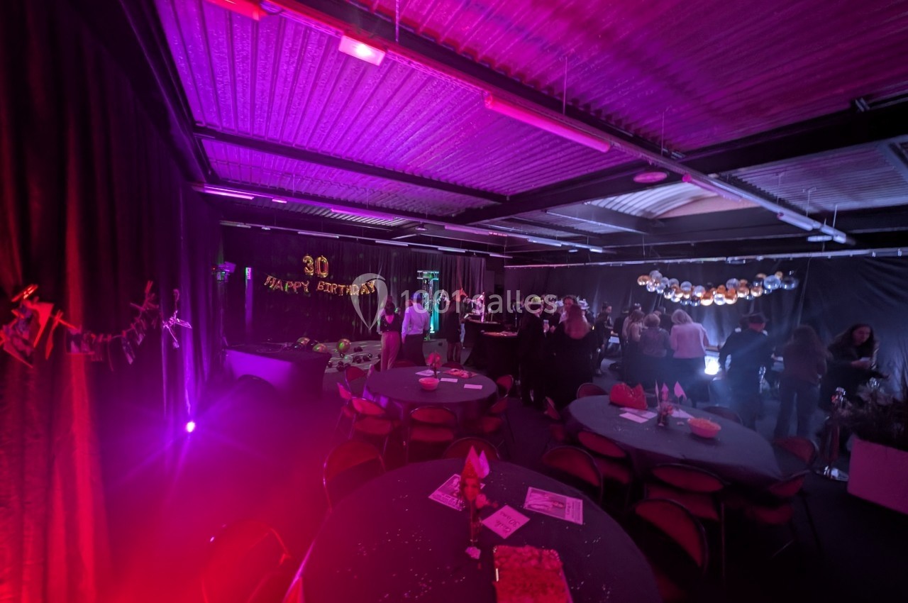 Salle décorée pour une fête d'anniversaire avec des tables rondes, guirlandes lumineuses et ambiance tamisée.