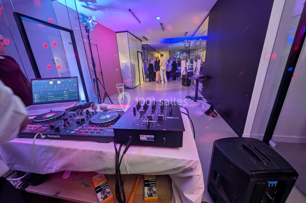 Poste de DJ avec platines et table de mixage au premier plan, soirée en cours dans une salle éclairée en arrière-plan.
