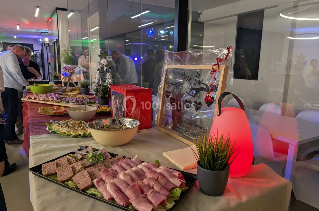 Buffet avec charcuterie, plats variés et décorations, dans une salle moderne éclairée pour un événement.