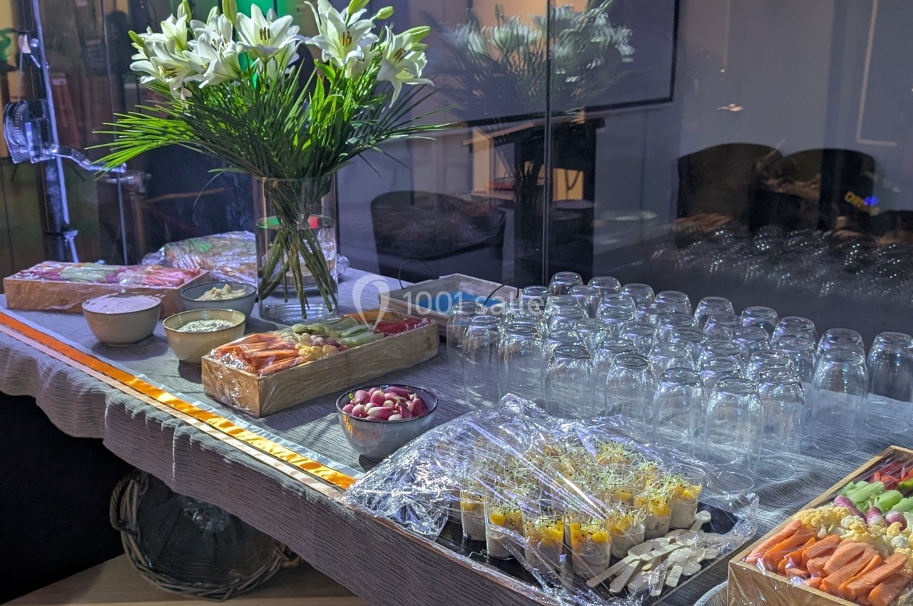 Table de buffet avec verrines, légumes, charcuterie, pains, fleurs blanches en vase et rangée de verres vides.
