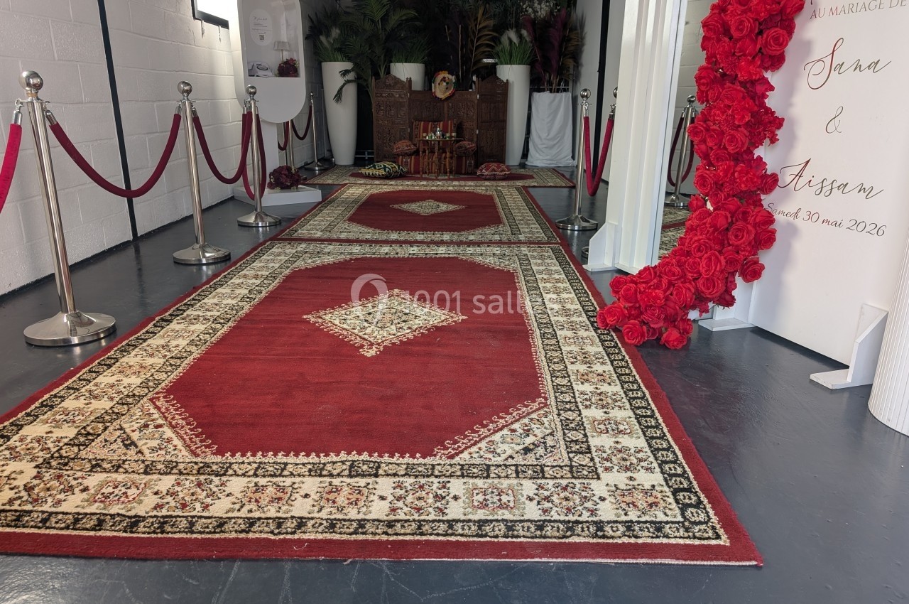 Tapis rouges décoratifs alignés dans une salle avec des fleurs rouges et un panneau de mariage en arrière-plan.