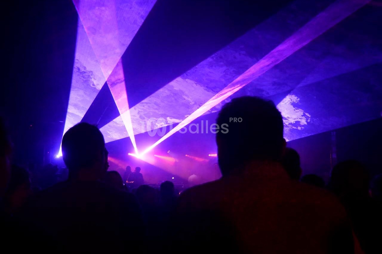 Silhouettes de personnes dans une salle sombre avec des faisceaux lumineux violets et bleus traversant la scène.