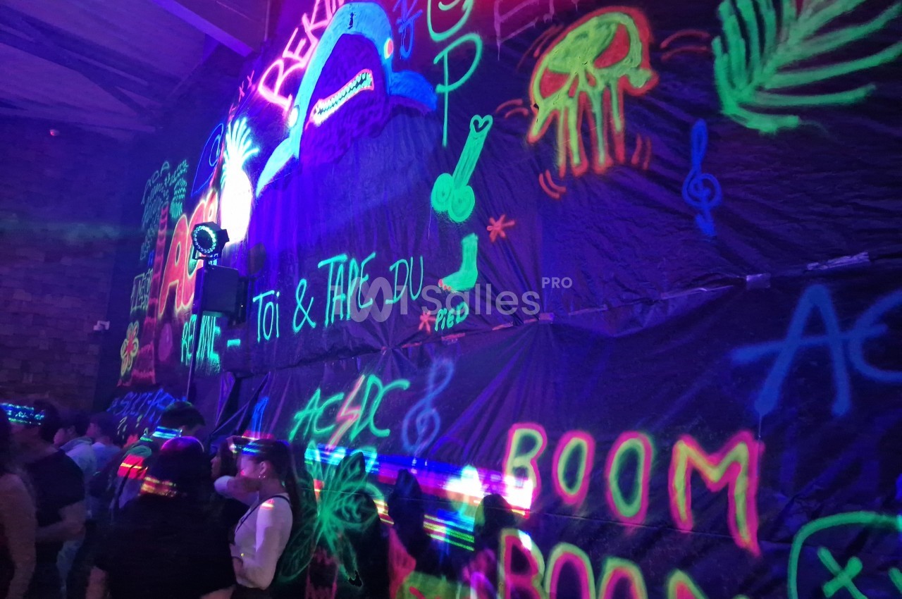 Mur décoré de graffitis fluorescents sous lumière noire, avec des personnes rassemblées au premier plan.