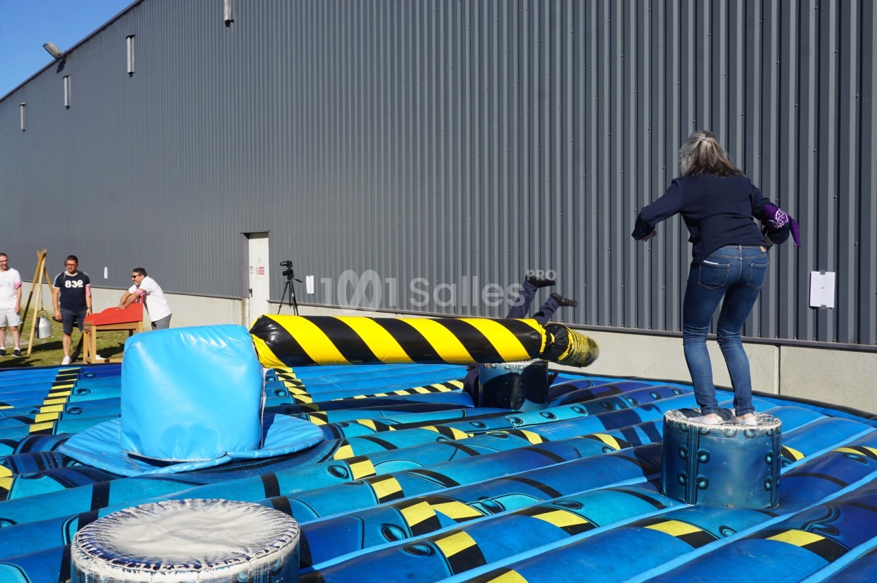 Personnes participant à un jeu gonflable où elles évitent une barre rotative dans un espace extérieur.