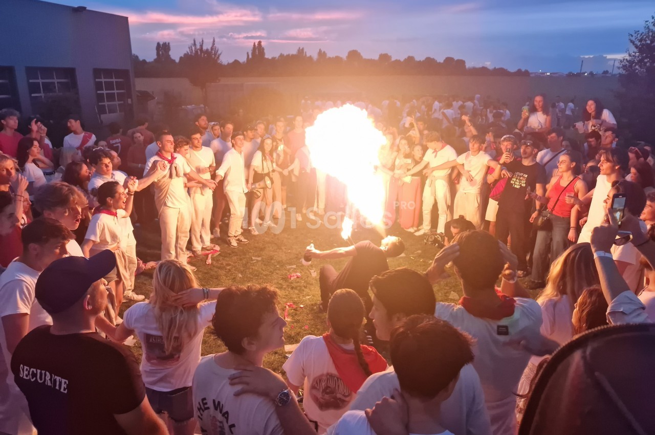 Un artiste cracheur de feu performe au centre d'un cercle de spectateurs lors d'un événement en extérieur au crépuscule.