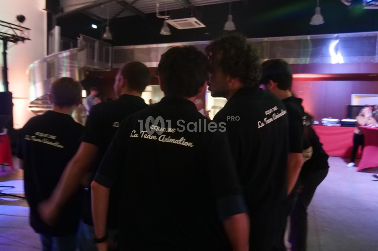 Un groupe de personnes portant des polos noirs avec l'inscription ’La Team Animation’ dans un espace intérieur éclairé.