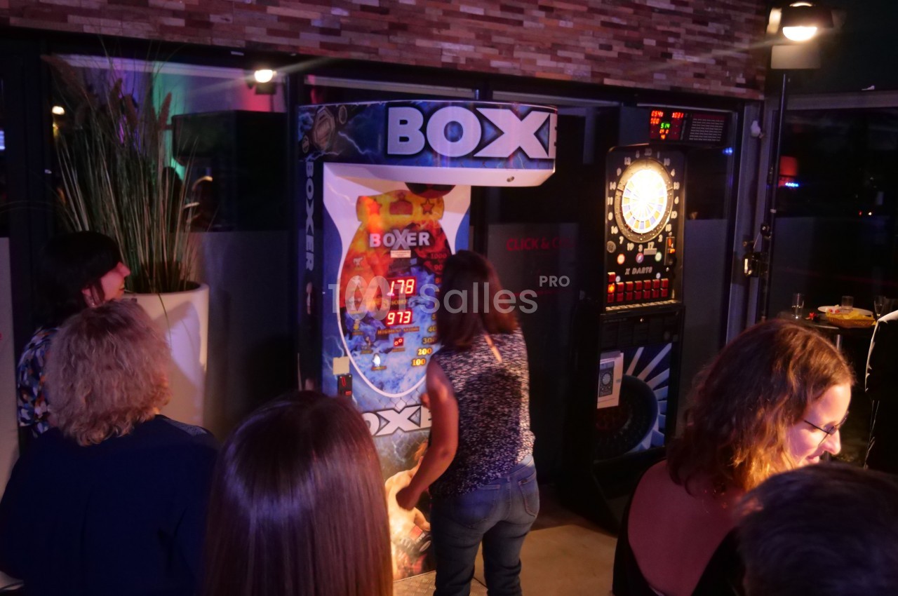 Une femme frappe une borne de punching-ball dans un espace intérieur, entourée de spectateurs.