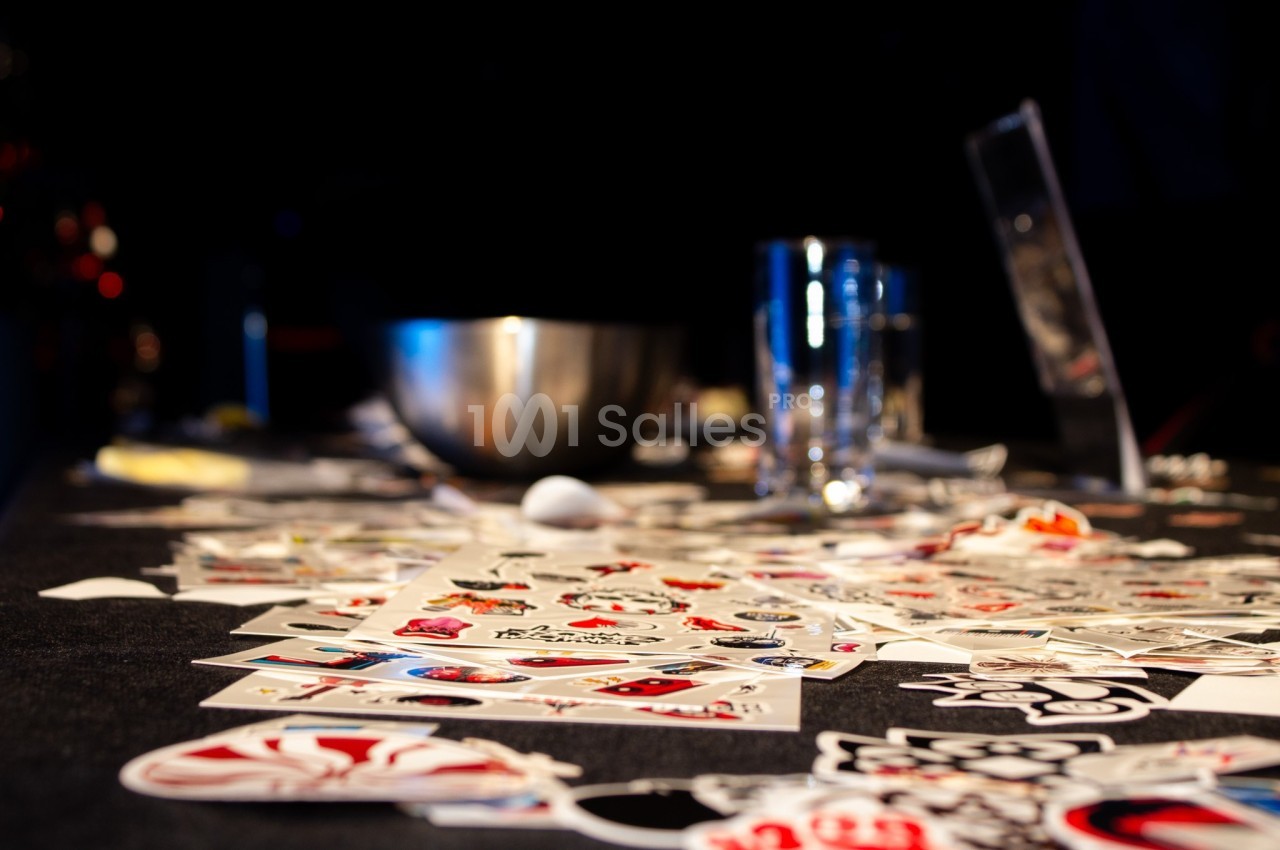 Cartes colorées éparpillées sur une table sombre avec un bol métallique et des verres en arrière-plan.
