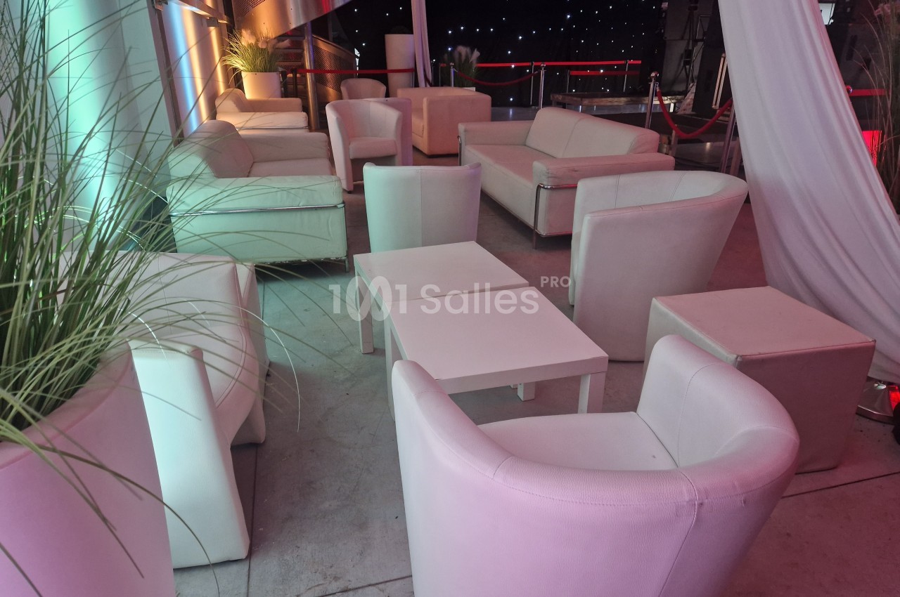 Mobilier de salon blanc avec tables basses, disposé sur une terrasse éclairée de lumières colorées et étoilées.