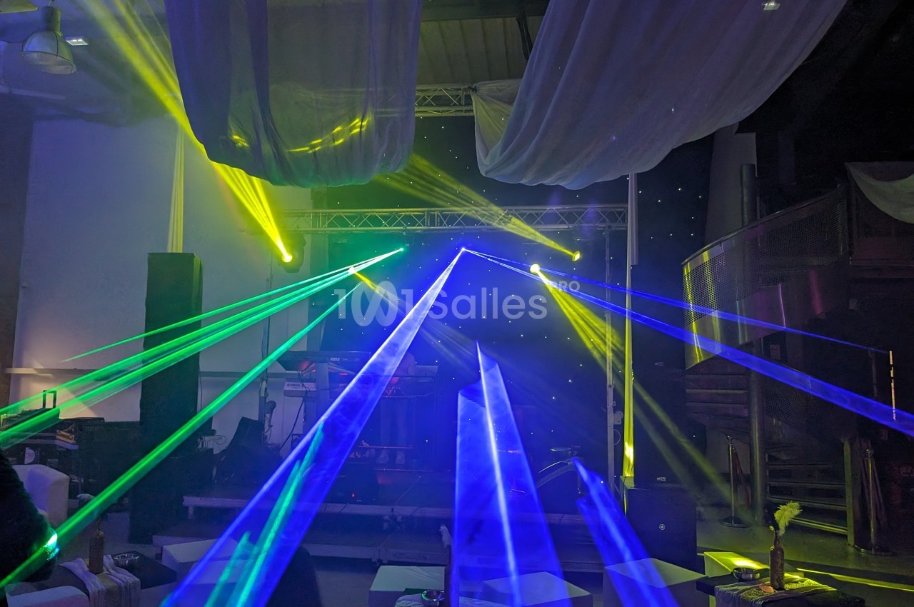 Jeux de lumières colorées avec des lasers verts et bleus illuminant une scène dans une salle décorée de voilages.