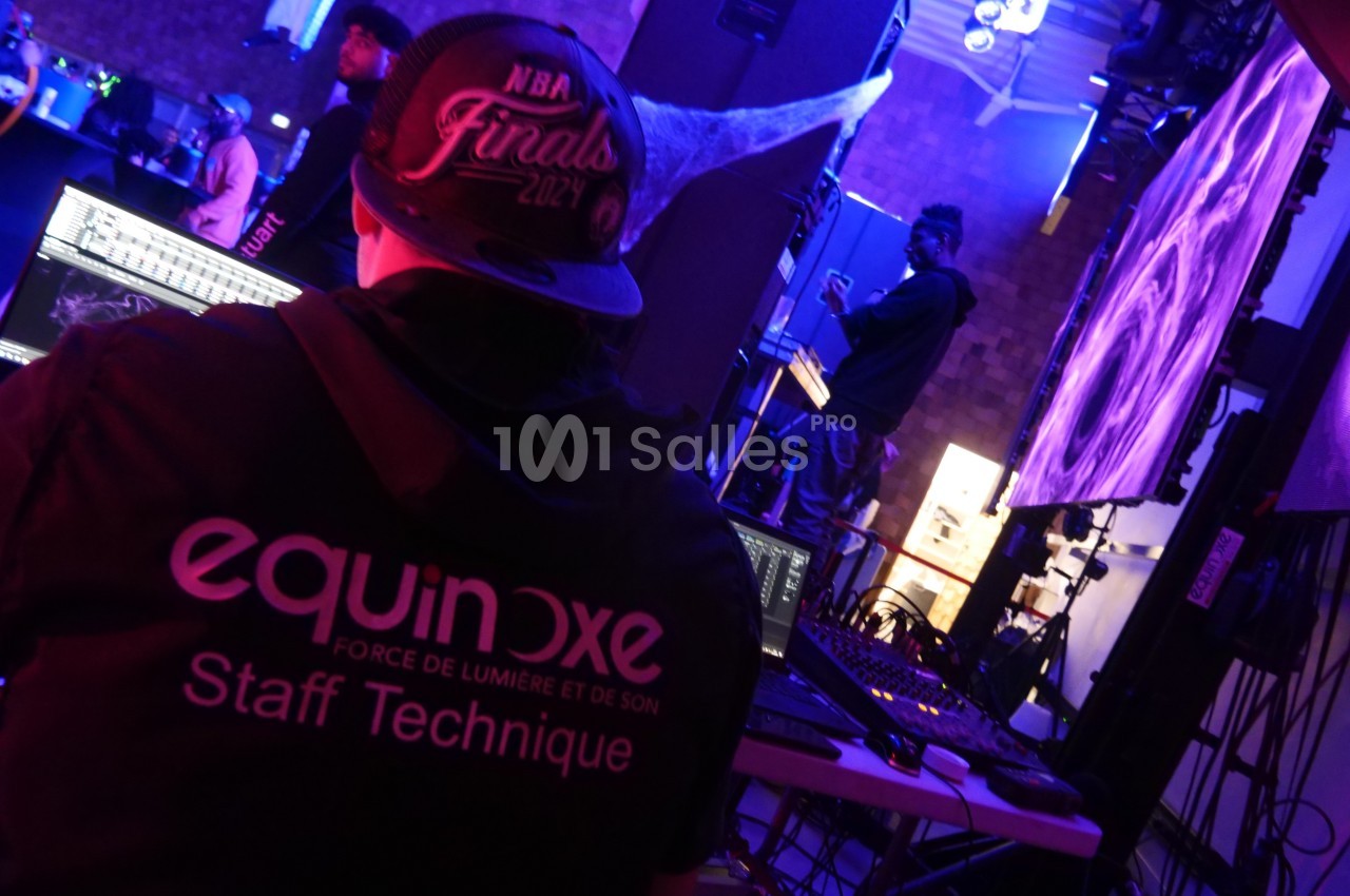 Technicien en régie supervisant des équipements audiovisuels lors d'un événement en intérieur avec éclairages colorés.