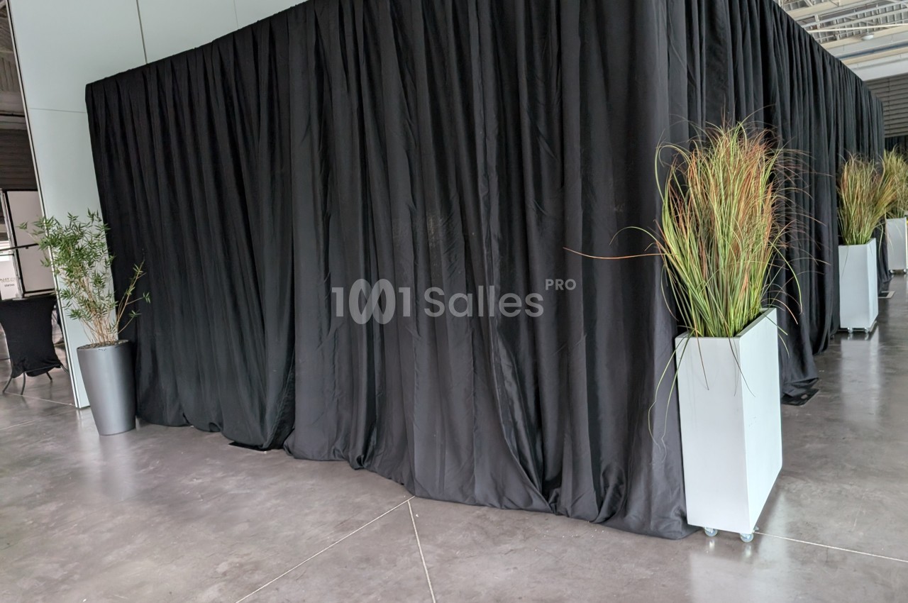 Rideaux noirs couvrant une structure, encadrés par des plantes en pots blancs sur un sol en béton.