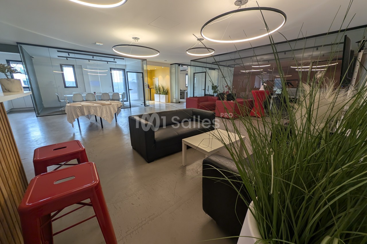 Espace intérieur moderne avec canapés noirs, tabourets rouges, plantes et grandes baies vitrées.