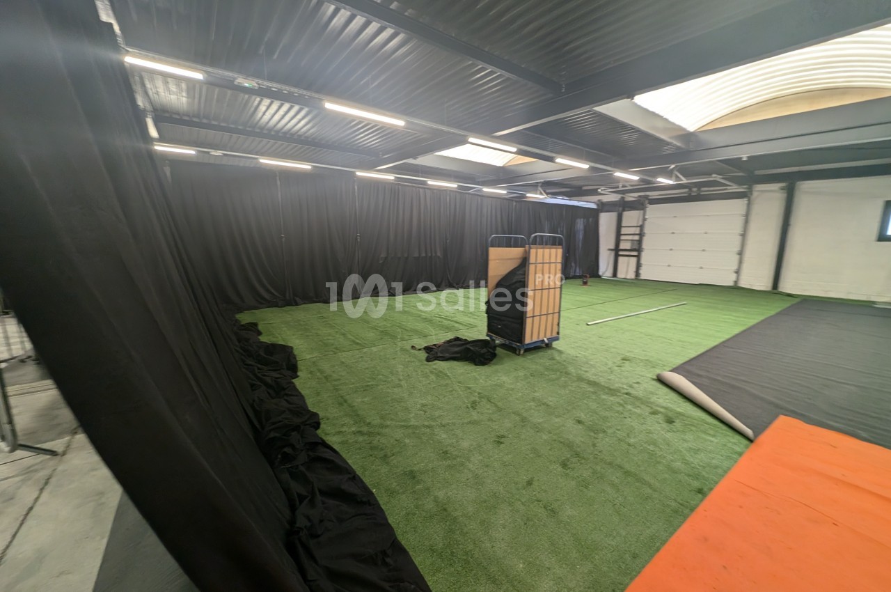 Salle intérieure avec sol en gazon synthétique, rideaux noirs, éclairage au plafond et matériel de rangement au centre.