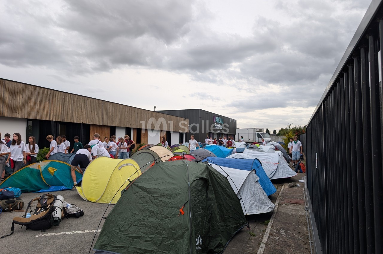 Tentes installées sur un parking devant un bâtiment, avec des personnes regroupées en arrière-plan.