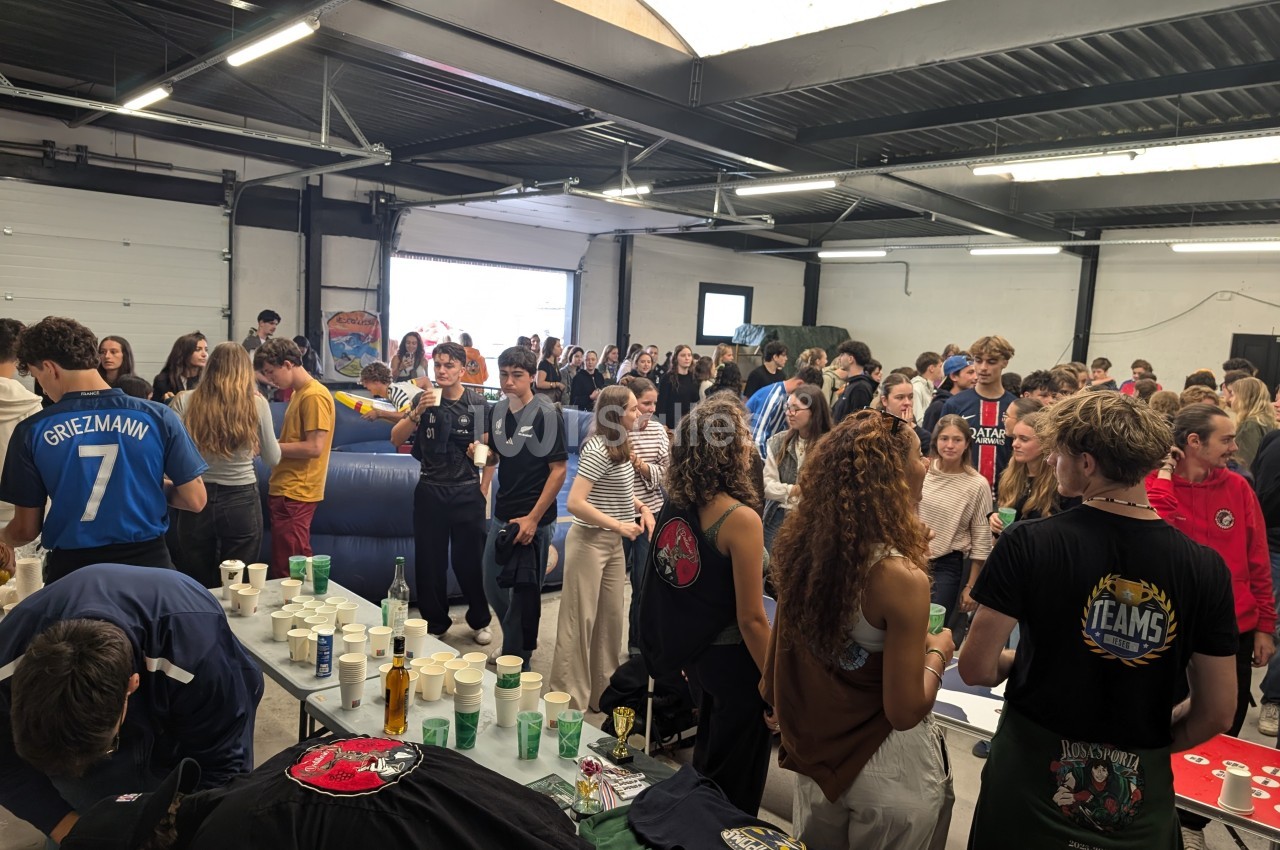 Groupe de personnes rassemblées dans un espace intérieur, participant à une activité avec des tables remplies de gobelets et…