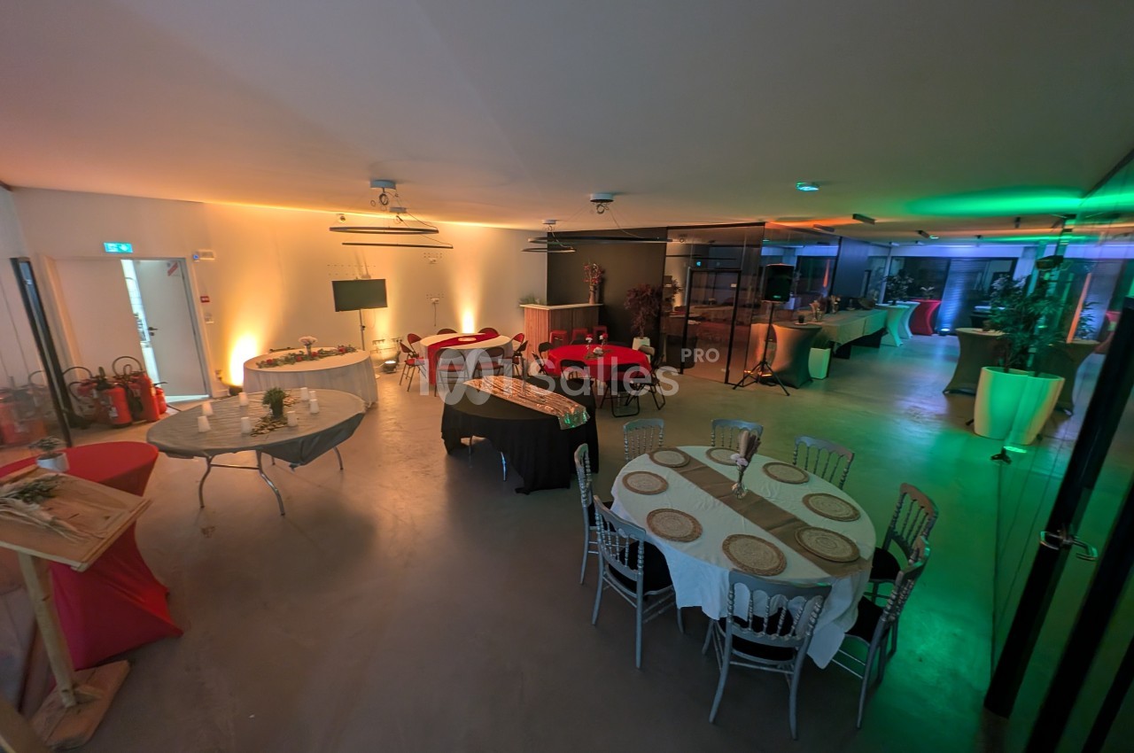 Salle aménagée pour un événement, avec tables rondes dressées, éclairage tamisé et décorations simples.