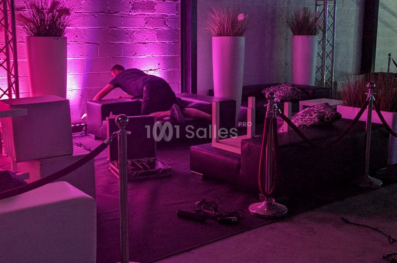 Un homme ajuste un canapé dans un espace intérieur décoré avec des lumières roses et des plantes en pots.