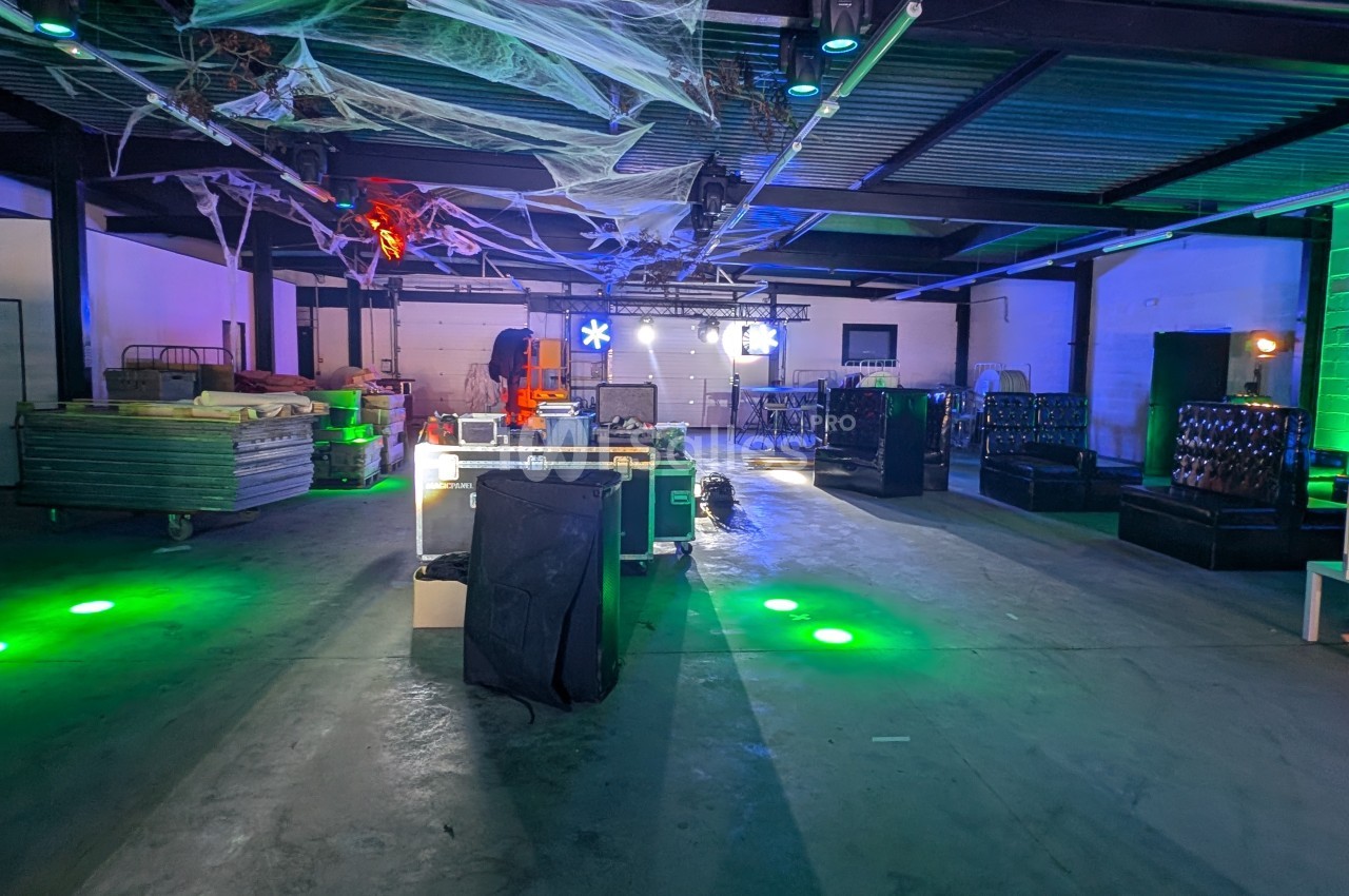 Entrepôt décoré pour un événement avec éclairage coloré, toiles d'araignée suspendues et mobilier disposé.