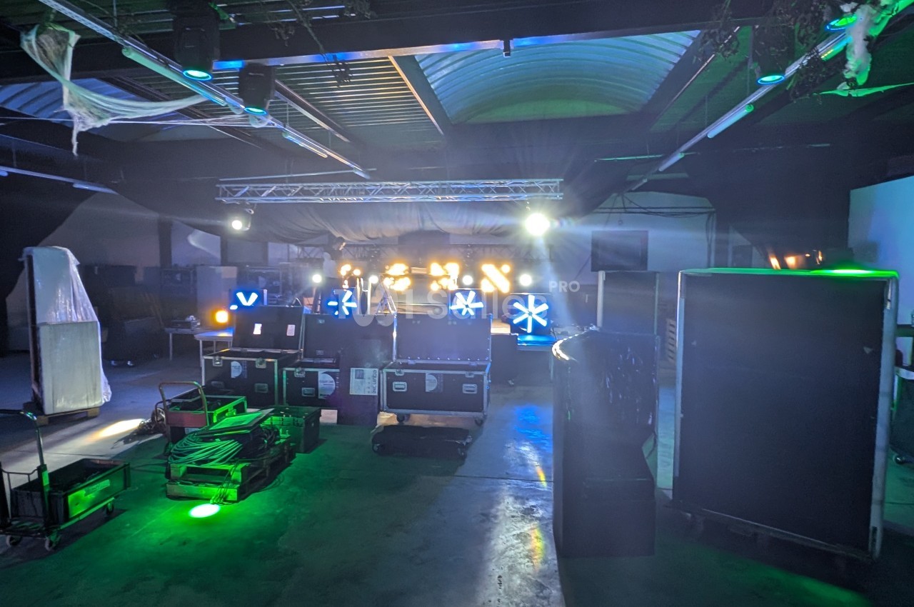 Salle sombre avec équipements de scène, projecteurs allumés et effets lumineux colorés en arrière-plan.
