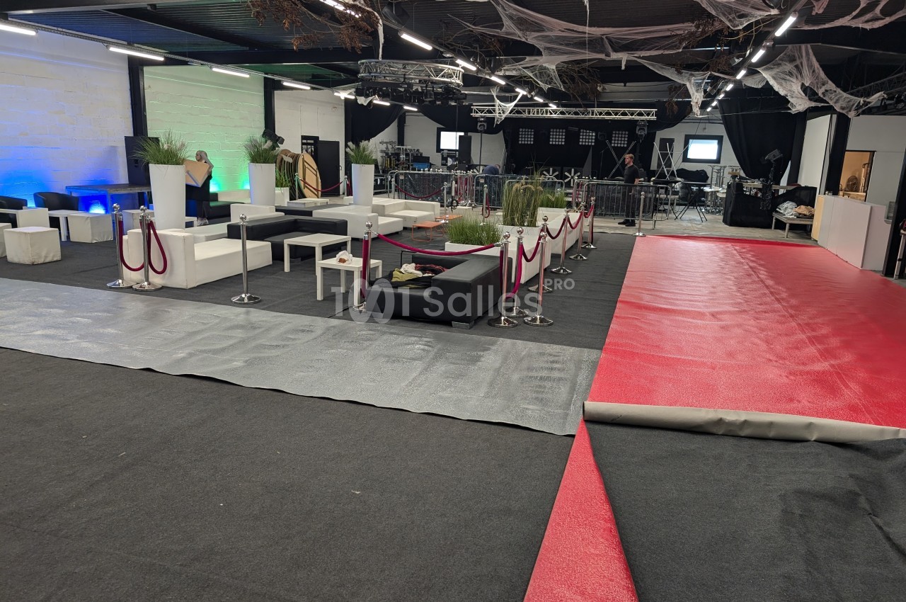 Salle en préparation avec tapis rouge partiellement déroulé, mobilier blanc et noir, et décorations suspendues.