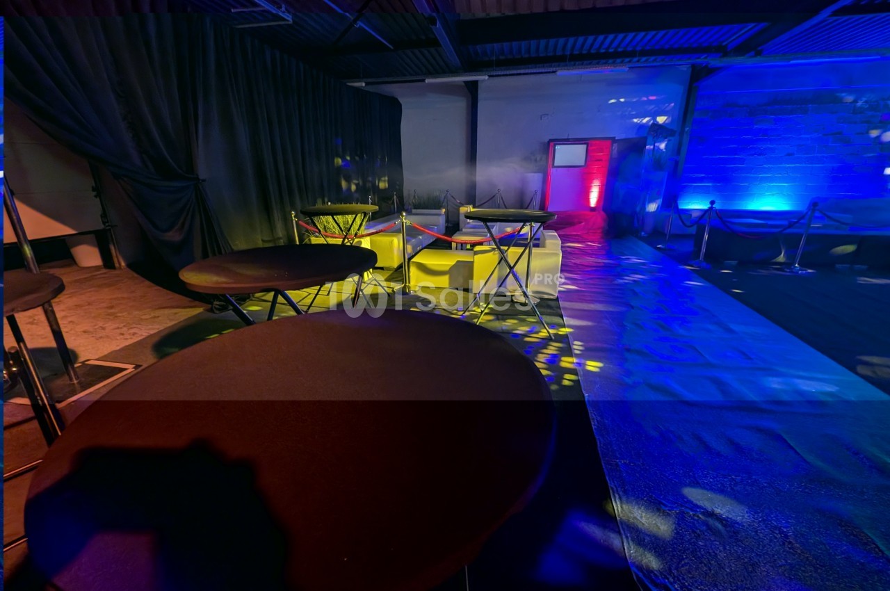 Salle décorée avec des tables hautes, éclairages colorés et rideaux noirs, ambiance événementielle.