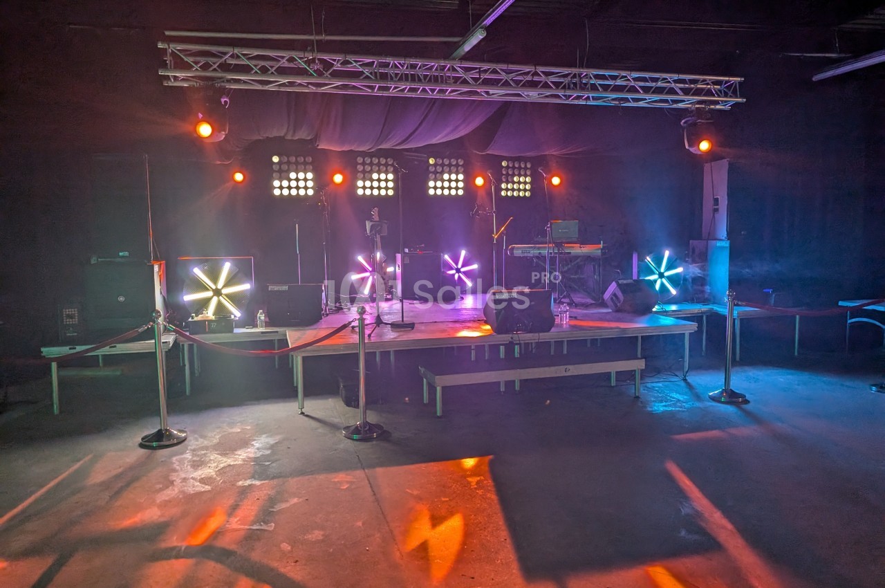 Scène vide éclairée par des projecteurs colorés dans une salle sombre avec des équipements audio visibles.