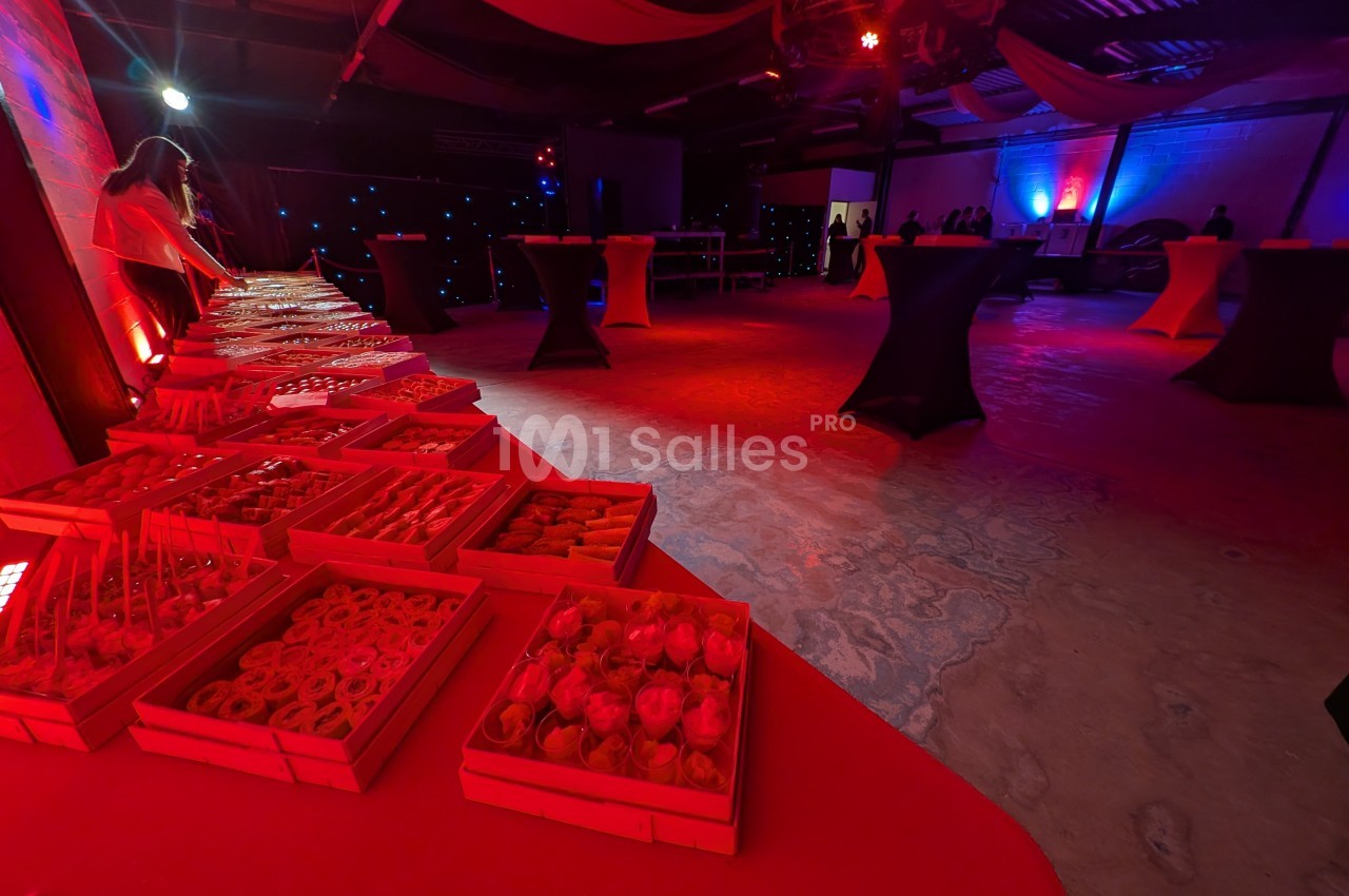 Salle de réception éclairée en rouge avec un buffet de pâtisseries disposé sur des tables à l'avant-plan.